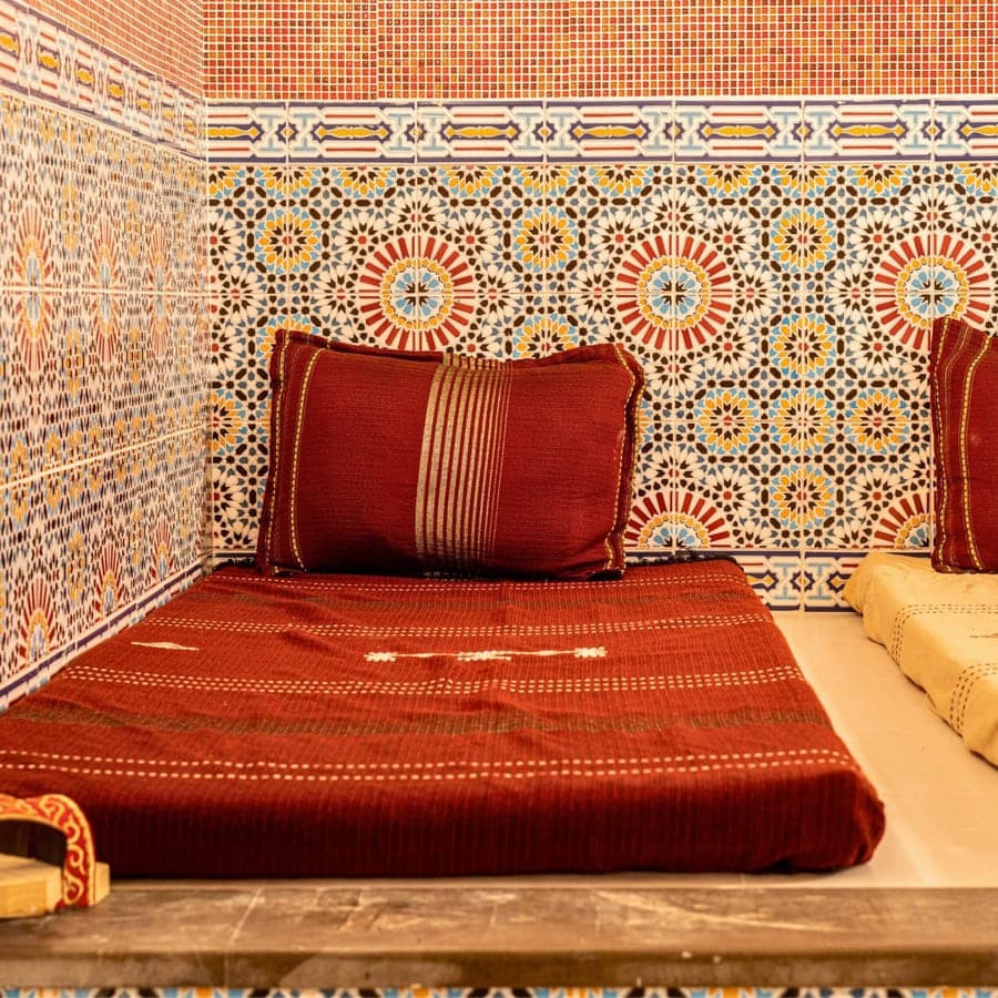Coussin brodé et babouches sur la banquette carrelée du hammam
