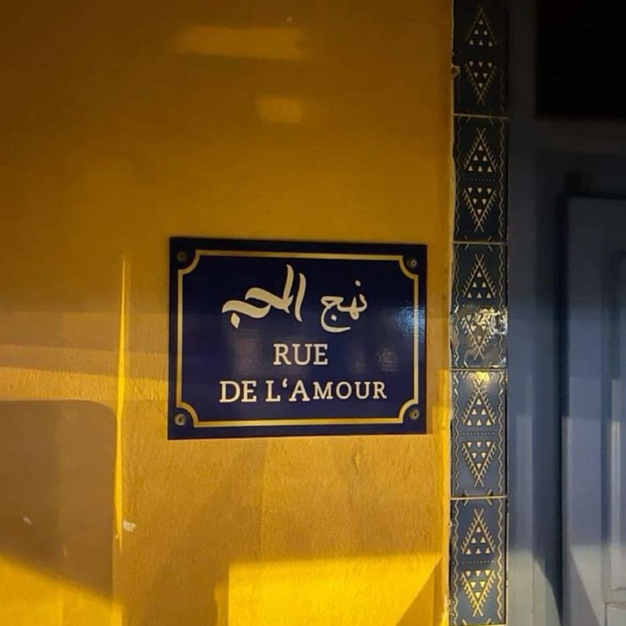 Plaque de rue bilingue la nuit, à côté d'un panneau de zellige