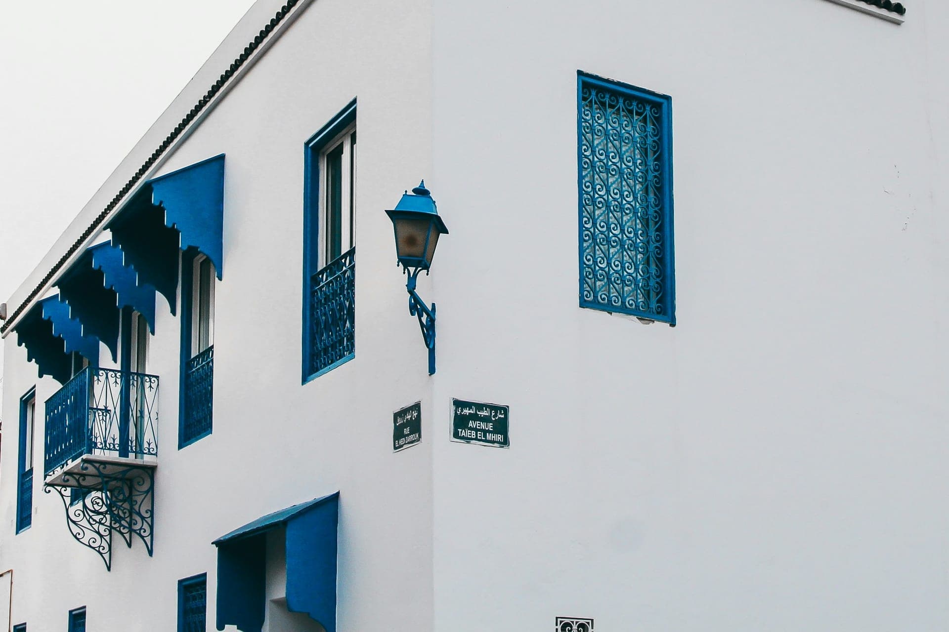Angle d'un bâtiment blanc avec fenêtres en fer forgé bleu, sous un ciel dégagé